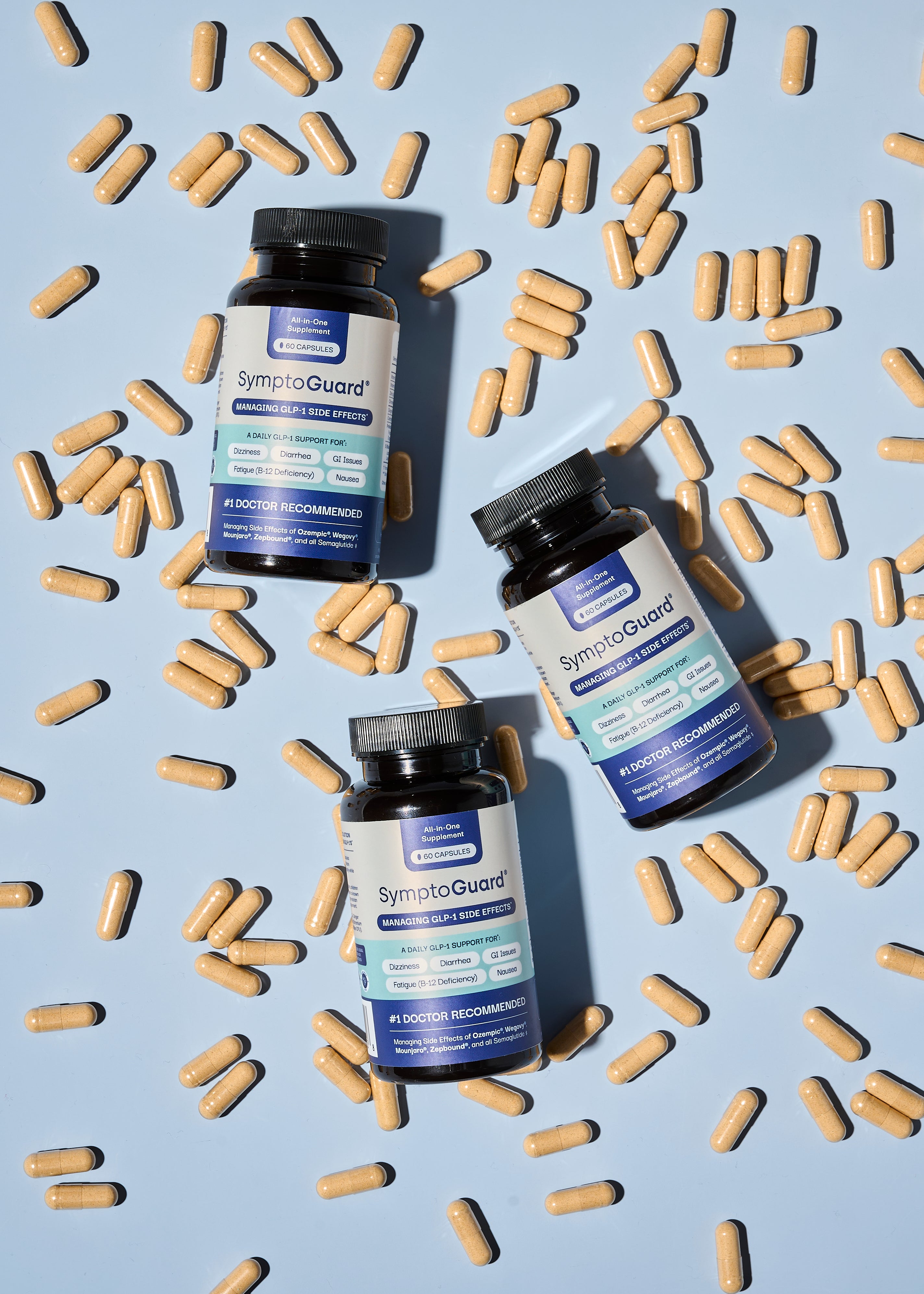 Three bottles of SymptoGuard lying flat on a scattered pile of supplement pills on a light blue background